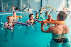 Aqua aerobics exercises, women with male trainer, indoor swimming pool.