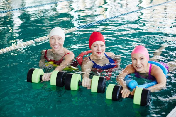 Three women with swimming barbells looking at camera from water during workout